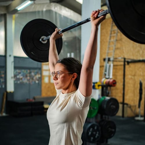 Woman performing a barbell overhead press with a barbell in a gym