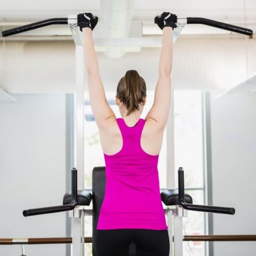 Woman gripping dip station handles for assisted pull-up exercise as a pull up alternative