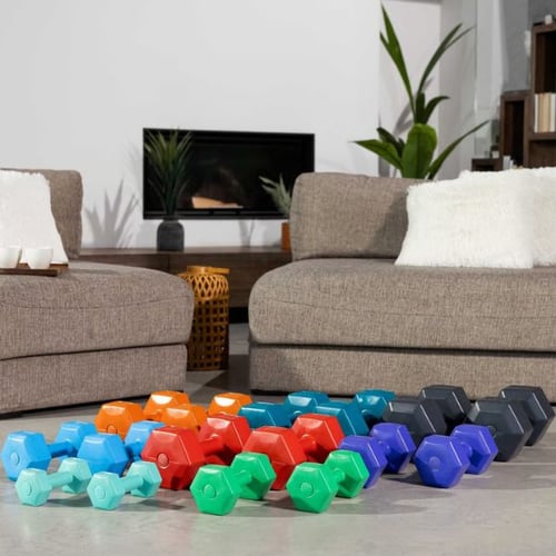 Collection of colorful Hop-Sport vinyl dumbbells arranged on the floor between sofas in a living room