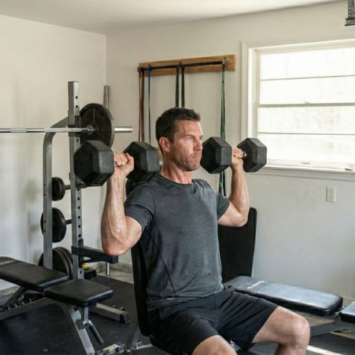 Man performing seated dumbbell shoulder press to build boulder shoulders at home gym