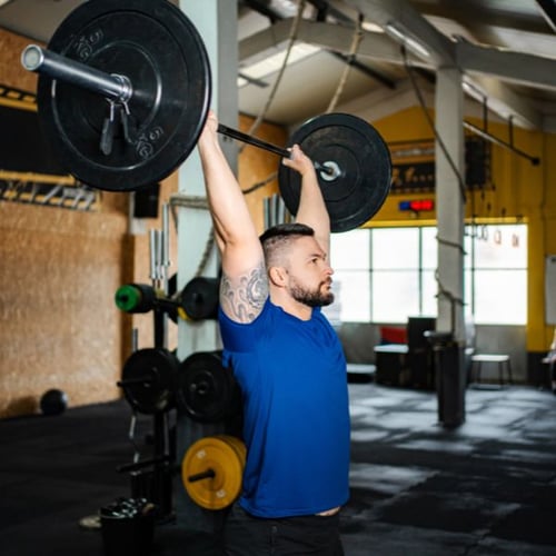 Man performing a barbell overhead press with a barbell in a gym