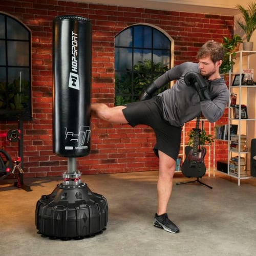 Man performs side kick on Hop-Sport free-standing punching bag in home gym setting