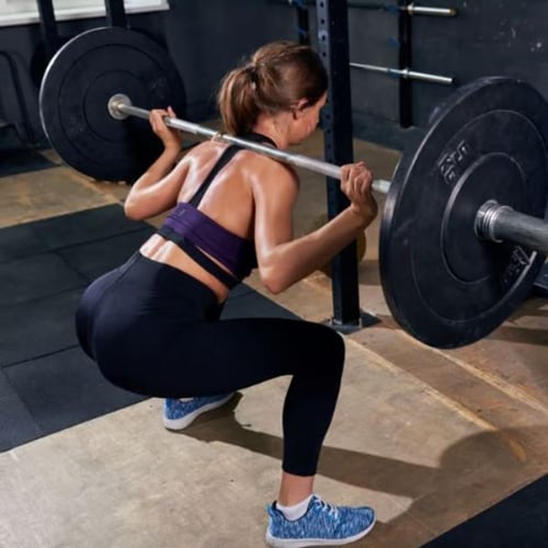 Woman performing barbell squat in gym