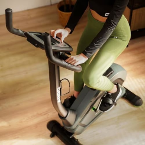 Woman using indoor upright exercise bike focusing on leg muscles worked during cycling