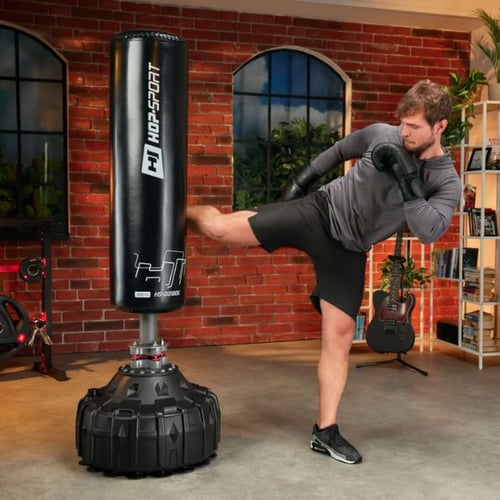 Man performing a side kick on a Hop-Sport free-standing punching bag in a workout room