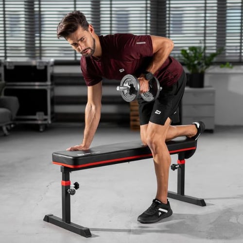 Man performing a one-arm dumbbell row using a flat Hop-Sport bench for support in a gym setting